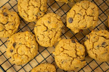 Várias cookies douradas e redondas com pepitas de chocolate negro salientes, dispostas sobre uma grelha de arrefecimento de metal.