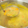 Prato fundo de barro com uma sopa cremosa de cor acastanhada, repleta de feijão verde cortado, meias-luas de cenoura laranja e feijões manteiga inteiros.