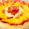 Tarte redonda assente num prato com pé, com uma base de massa folhada rústica e coberta de forma abundante e em espiral por fatias brilhantes de morangos vermelhos, pêssegos laranjas e ananás amarelo.