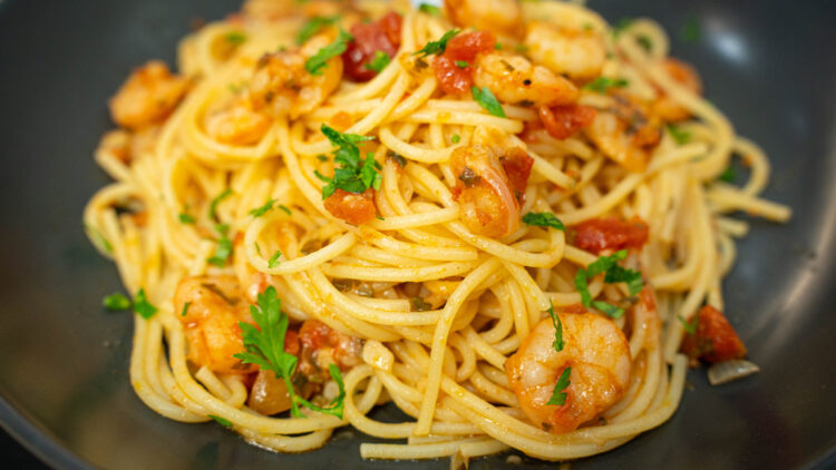 Prato elegante cheio de esparguete brilhante envolvido num molho de tomate rico, generosamente coberto com miolo de camarão cor-de-laranja, queijo parmesão derretido e pedacinhos de salsa verde picada.