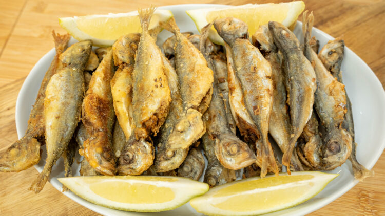 Travessa cheia de pequenos carapaus fritos e crocantes, divididos entre os mais claros de farinha de trigo e os mais dourados de farinha de milho, decorados com gomos de limão fresco.