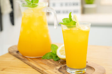 Jarra de vidro de 1 litro, suada devido ao gelo, cheia com uma bebida amarelo-alaranjada, decorada com fatias de limão e folhas verdes de hortelã fresca no topo.