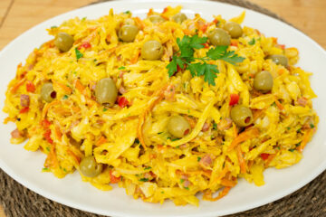 Travessa de servir recheada com Bacalhau à Assis muito cremoso e húmido, onde sobressaem os tons laranjas da cenoura e amarelos dos ovos, decorado no topo com um raminho de salsa fresca e azeitonas verdes recheadas com pimento.