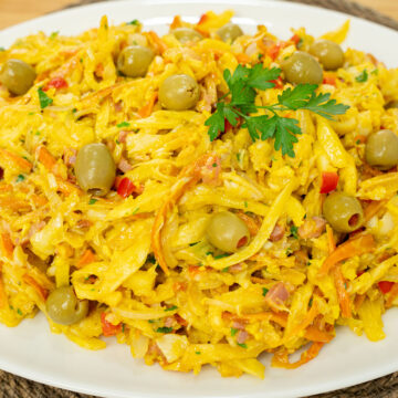 Travessa de servir recheada com Bacalhau à Assis muito cremoso e húmido, onde sobressaem os tons laranjas da cenoura e amarelos dos ovos, decorado no topo com um raminho de salsa fresca e azeitonas verdes recheadas com pimento.