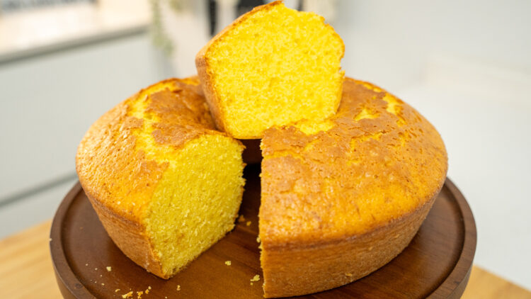 Um bolo de buraco clássico, com uma crosta dourada e perfeitamente cozida, desenformado sobre um prato branco de pé alto, pronto a ser servido.
