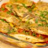 Travessa de vidro transparente com um suculento assado de forno, exibindo pedaços de peixe branco (solha) cozinhados sobre uma cama rica de rodelas finas de batata, cebola, tiras de pimento verde e fatias de tomate, tudo polvilhado com salsa fresca picada.