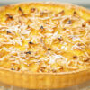 Tarte redonda rústica de 27 centímetros disposta num prato de servir, com rebordos de massa dourada, cobertura densa de pedaços de ameixa amarela cozida e lascas de amêndoa palitada tostada, salpicada com açúcar em pó.