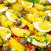 Uma rústica travessa de barro retangular, cheia de um prato gratinado com camadas de batata e peixe, decorada no topo com metades de ovo cozido, azeitonas pretas e salsa picada.