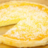 Tarte redonda com uma base de massa folhada dourada e estaladiça, revelando um interior amarelo-claro e húmido, desenformada e servida num prato elegante.