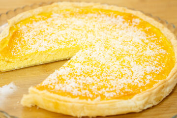Tarte redonda com uma base de massa folhada dourada e estaladiça, revelando um interior amarelo-claro e húmido, desenformada e servida num prato elegante.