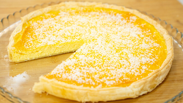 Tarte redonda com uma base de massa folhada dourada e estaladiça, revelando um interior amarelo-claro e húmido, desenformada e servida num prato elegante.