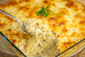 Travessa retangular de vidro cheia de bacalhau com natas, acabada de sair do forno, com uma crosta generosa de queijo mozarela derretido e gratinado num tom dourado irresistível.