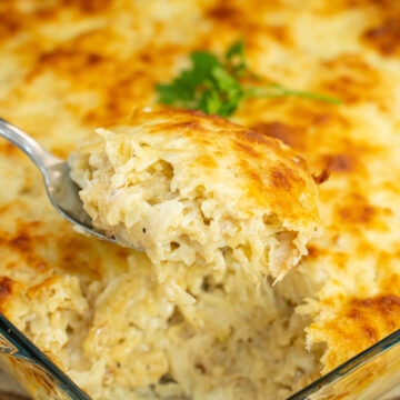 Travessa retangular de vidro cheia de bacalhau com natas, acabada de sair do forno, com uma crosta generosa de queijo mozarela derretido e gratinado num tom dourado irresistível.