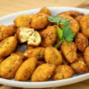 Uma travessa branca repleta de pastéis de pescada perfeitamente fritos, com uma cor dourada uniforme e formato tradicional alongado, repousando sobre uma cama de papel absorvente.
