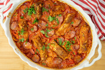 Travessa rústica de barro repleta de arroz assado com um tom dourado escuro, guarnecido no topo com pedaços de entrecosto de porco suculentos, rodelas de chouriço, tiras de pimento vermelho e polvilhado com salsa fresca picada.