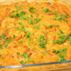 Travessa de vidro quadrada saída do forno, contendo filetes de peixe brancos envoltos num molho cremoso e espesso de cor alaranjada, pontilhado por finas tiras de pimento verde e generosamente polvilhado com salsa fresca picada.