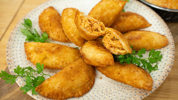Prato tradicional com rissóis de frango caseiros dourados e crocantes, cortados ao meio para revelar o recheio cremoso, servidos ao lado de uma travessa de arroz de tomate malandrinho.