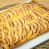Tarte retangular de massa folhada, exibindo um rebordo alto, dourado e estaladiço, com um interior recheado de creme amarelo coberto por finas meias-luas de maçã assada e brilhante (pincelada com mel).