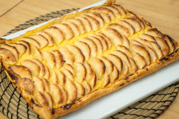 Tarte retangular de massa folhada, exibindo um rebordo alto, dourado e estaladiço, com um interior recheado de creme amarelo coberto por finas meias-luas de maçã assada e brilhante (pincelada com mel).