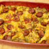 Travessa rústica de barro cheia de arroz carolino cozinhado no forno, com uma tonalidade alaranjada do açafrão, coberto com pedaços de frango do campo dourados, pimentos e rodelas de chouriço tostadas.