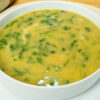 Tigela de louça branca com sopa de nabiças quente e fumegante, destacando o creme alaranjado salpicado com folhas verdes de nabiça e grãos inteiros de feijão manteiga, regada com um fio de azeite.