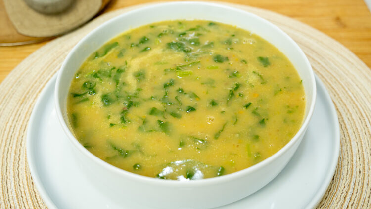 Tigela de louça branca com sopa de nabiças quente e fumegante, destacando o creme alaranjado salpicado com folhas verdes de nabiça e grãos inteiros de feijão manteiga, regada com um fio de azeite.