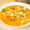 Prato fundo servindo uma porção generosa de arroz caldoso com pedaços de pota, pescada e camarão num molho avermelhado rico, polvilhado com salsa fresca picada.