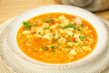 Prato fundo servindo uma porção generosa de arroz caldoso com pedaços de pota, pescada e camarão num molho avermelhado rico, polvilhado com salsa fresca picada.