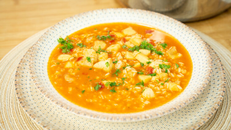 Prato fundo servindo uma porção generosa de arroz caldoso com pedaços de pota, pescada e camarão num molho avermelhado rico, polvilhado com salsa fresca picada.