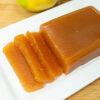 Taças cheias de marmelada caseira firme, acompanhadas por frascos de vidro invertidos contendo geleia de marmelo com uma cor âmbar vibrante e translúcida.