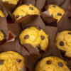 Muffins de abóbora caseiros e dourados dispostos numa travessa laranja temática, com pepitas de chocolate visíveis no topo e uma textura visivelmente fofa.