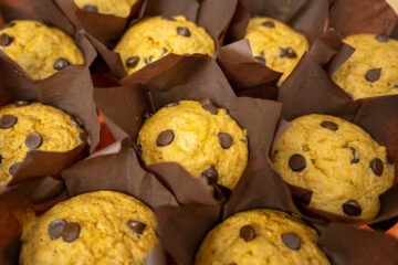 Muffins de abóbora caseiros e dourados dispostos numa travessa laranja temática, com pepitas de chocolate visíveis no topo e uma textura visivelmente fofa.