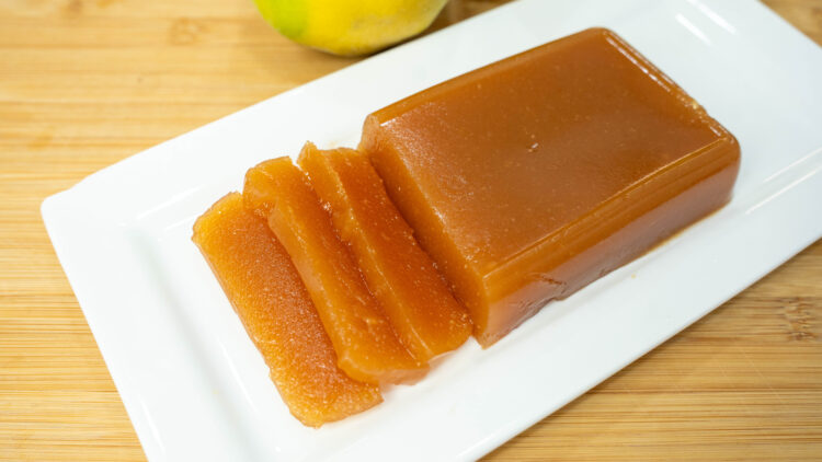 Taças cheias de marmelada caseira firme, acompanhadas por frascos de vidro invertidos contendo geleia de marmelo com uma cor âmbar vibrante e translúcida.